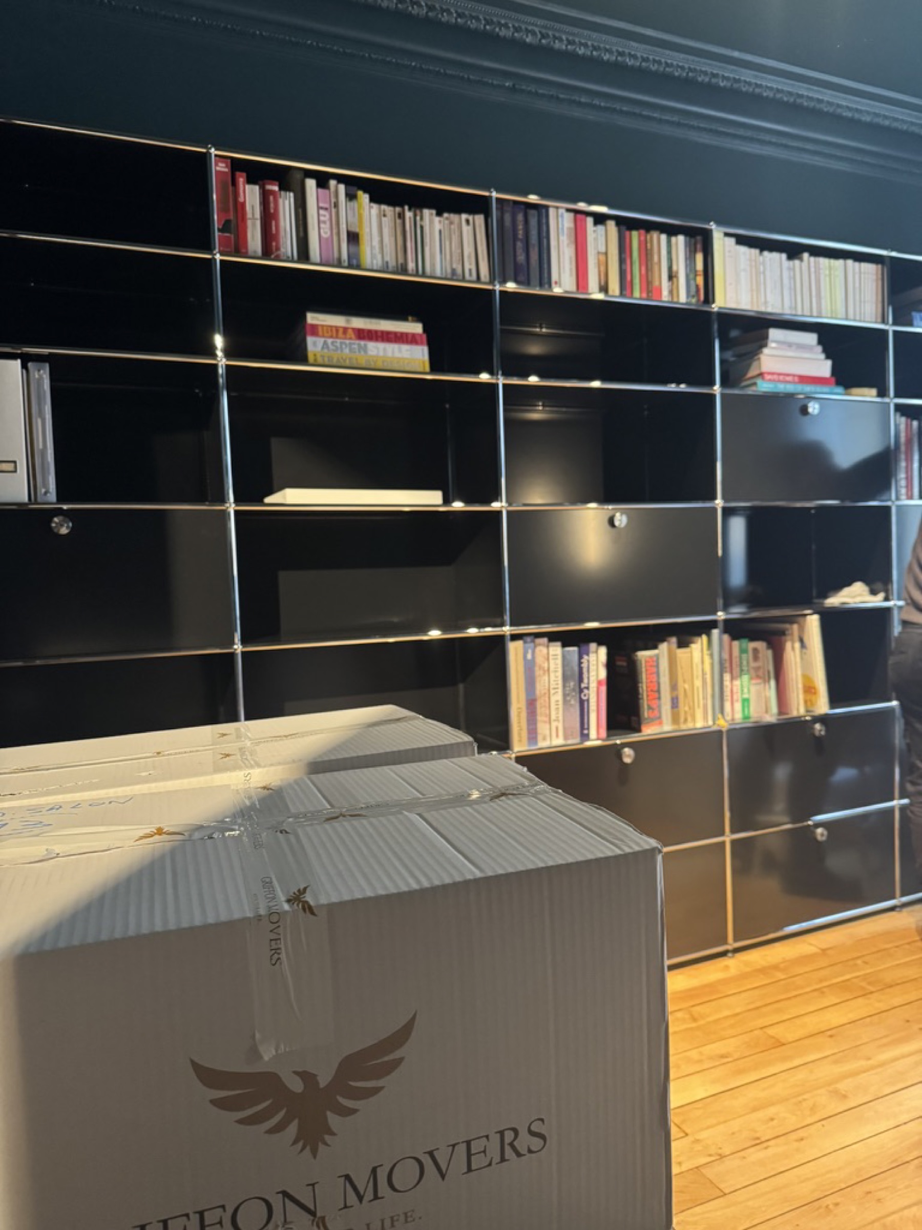 Bibliothèque USM Haller noire avec collection de livres et cartons signés Griffon Movers en avant-plan, déménagement résidentiel haut de gamme