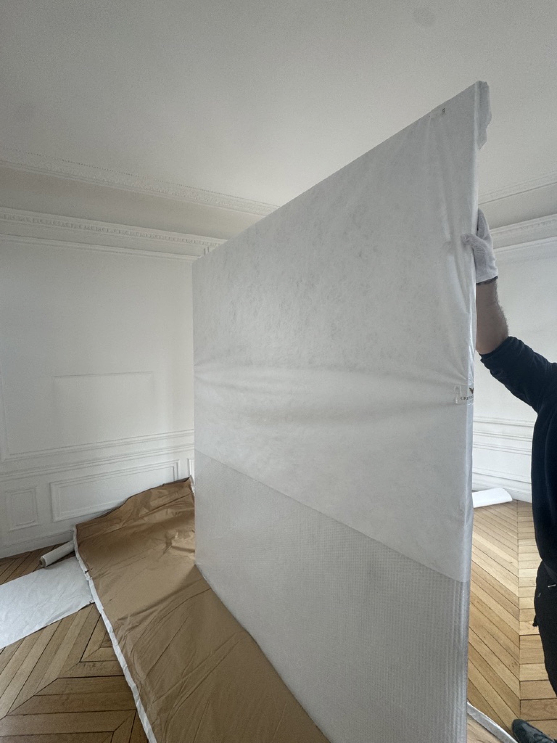 Déménageur Griffon Movers protégeant un grand tableau encadré avec une housse de conservation dans un salon haussmannien parisien à parquet point de Hongrie